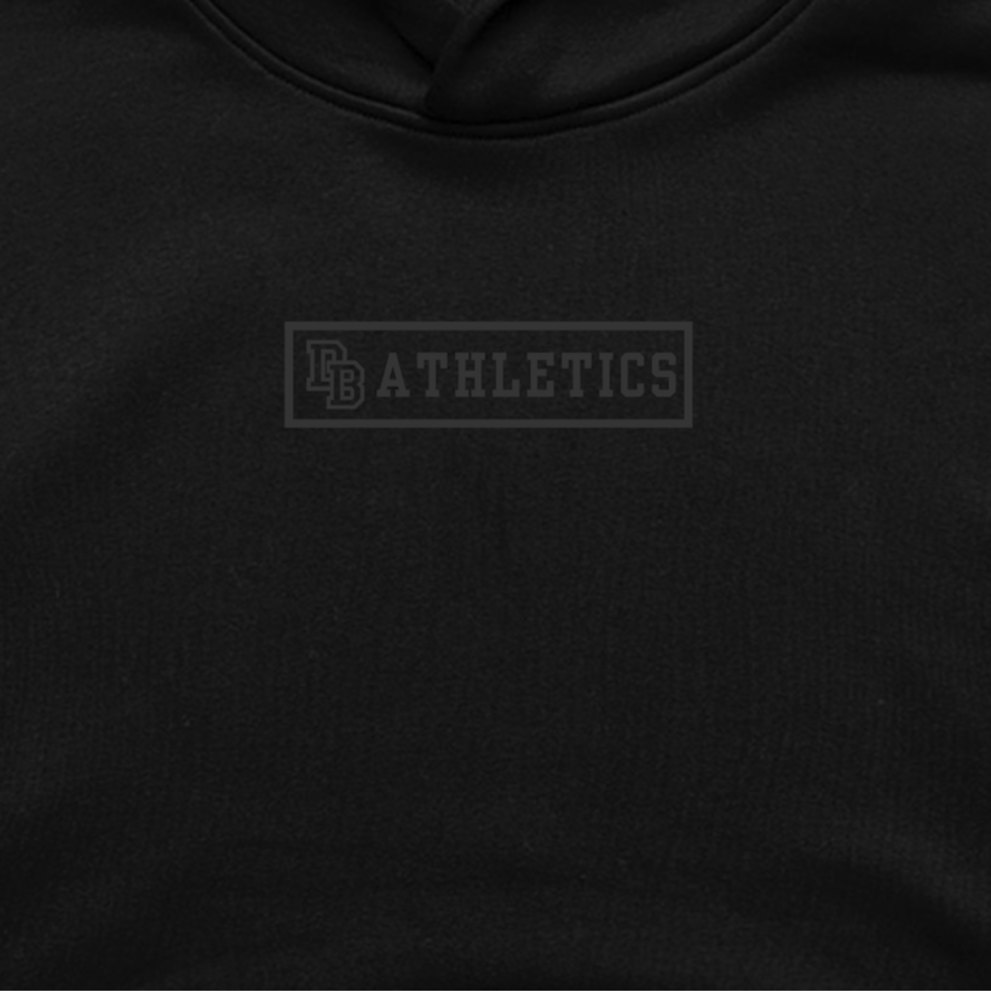 Close-up of The Issue Hoodie — black heavyweight fleece with matte black DB Athletics Brick vinyl emblem, minimal tone-on-tone design from the Varsity Drop Collection.