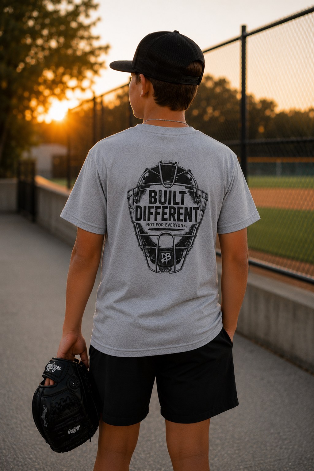 Person wearing a gray t-shirt with 'Built Different' design, standing on a path with sunset in the background.